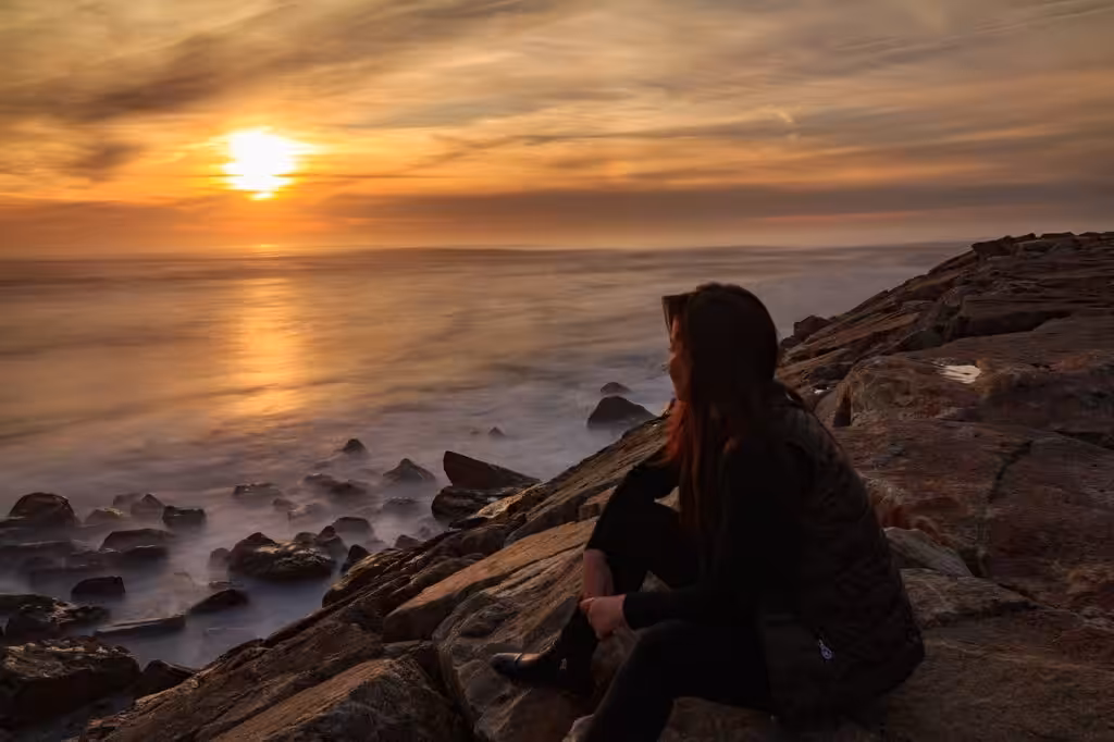 Frau sitzt am Meer beim Sonnenuntergang
