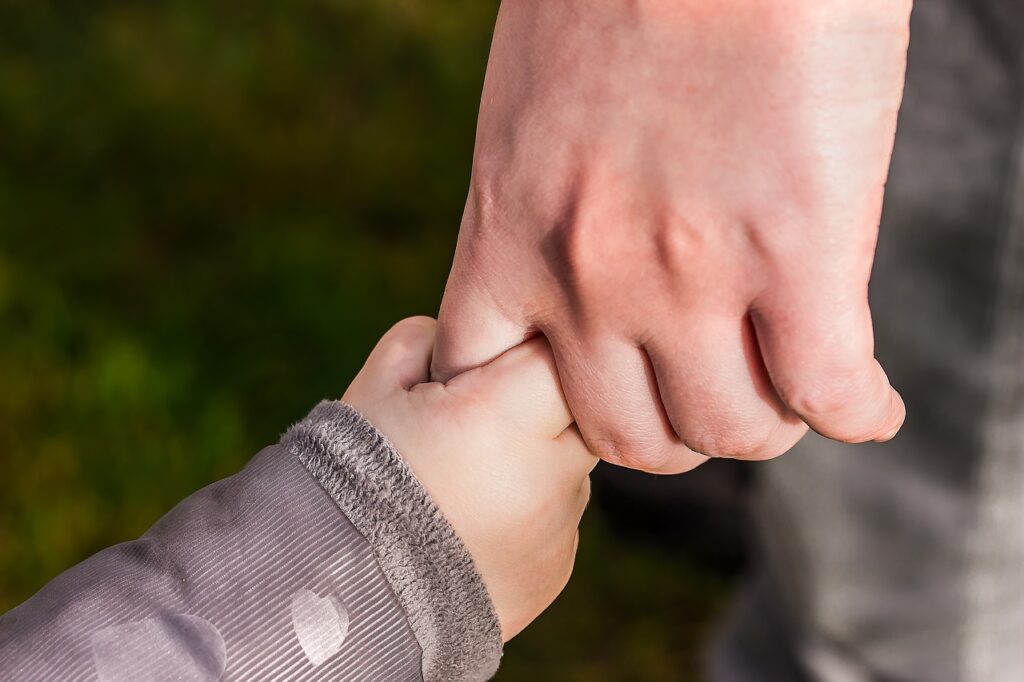Neurodiversität und Trauma im Business: Traumasensibles Coaching Karen Wiltner Coaching Hände eines Erwachsenen und eines Kindes halten sich fest, symbolisiert die Prägung durch Kindheitserfahrungen und emotionale Blockaden.